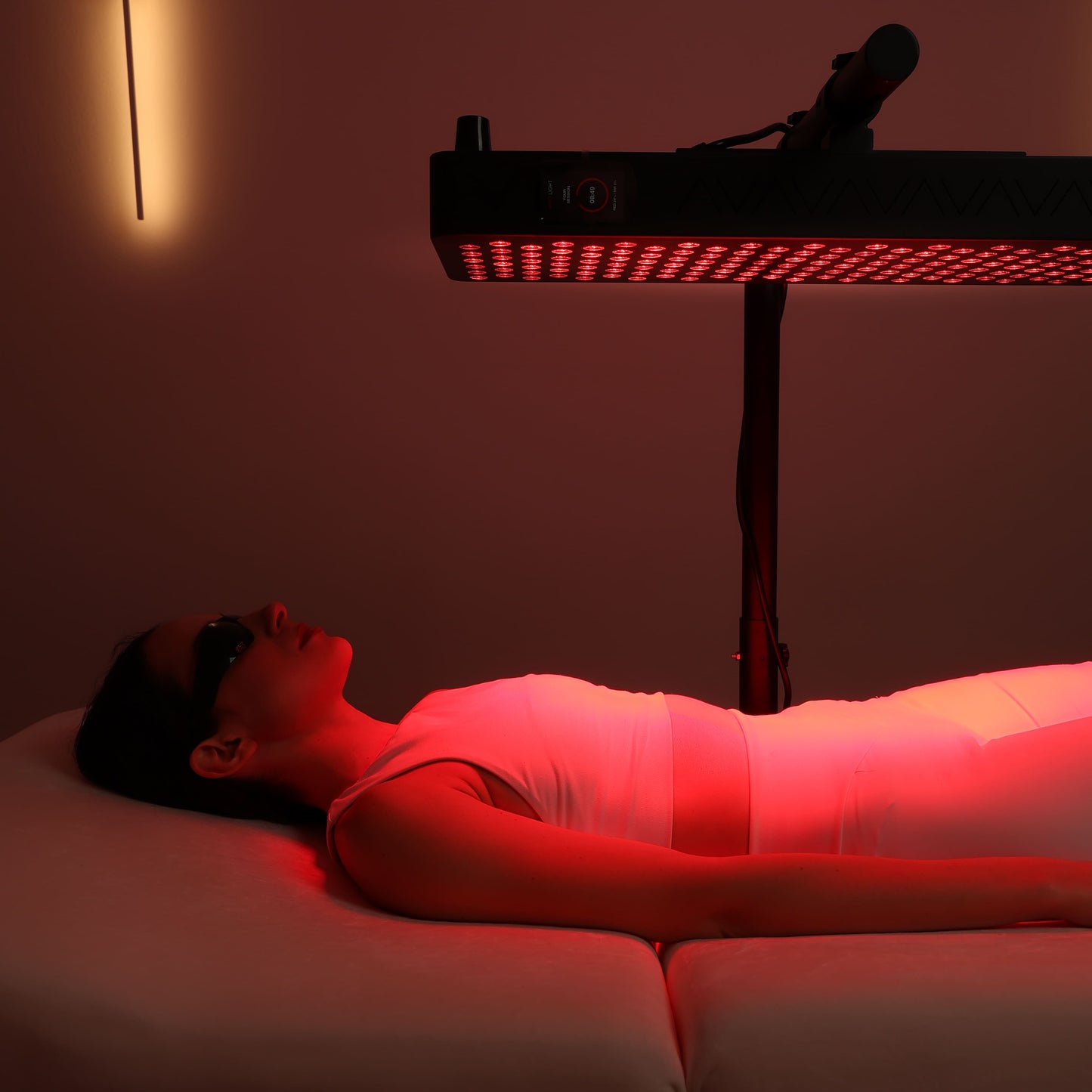 Woman lying under a full-body red light therapy panel during treatment