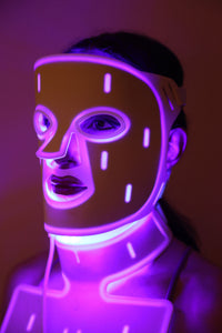 Close-up of woman wearing a red light therapy face and neck mask with purple light